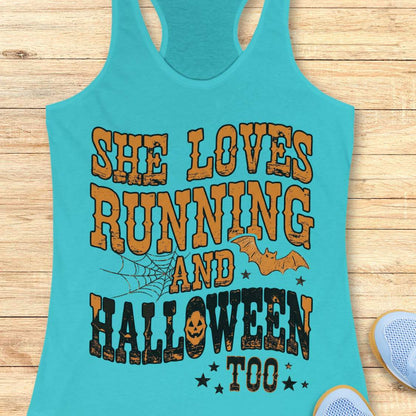 A blue racerback tank top laid flat on a light wood plank background, featuring a large Halloween-themed graphic that reads 'SHE LOVES RUNNING AND HALLOWEEN TOO' in orange and black distressed lettering, with spiderwebs, bats, and stars.