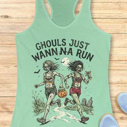A mint racerback tank top laid flat on a light wood surface, featuring a Halloween graphic of two zombie runners with the text 'GHOULS JUST WANNNA RUN' and a jack-o'-lantern. Part of a blue shoe is visible at the bottom right.