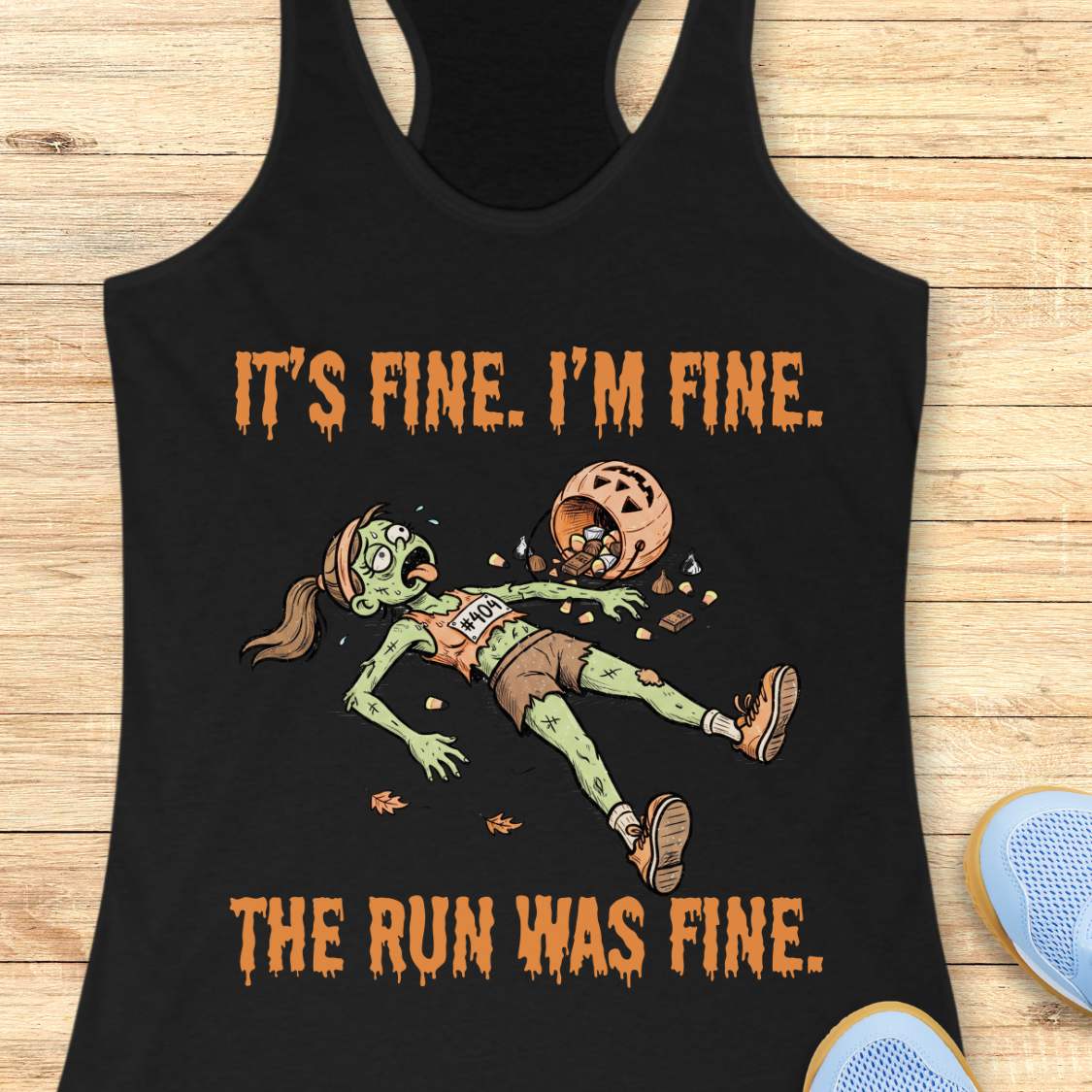 A black racerback tank top laid flat on a light wood surface, featuring a zombie running graphic with the text 'IT'S FINE. I'M FINE.