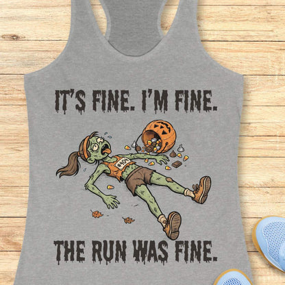 A heather gray racerback tank top laid flat on a light wood surface, featuring a zombie running graphic with the text 'IT'S FINE. I'M FINE.