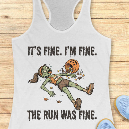 A white racerback tank top laid flat on a light wood surface, featuring a zombie running graphic with the text 'IT'S FINE. I'M FINE.
