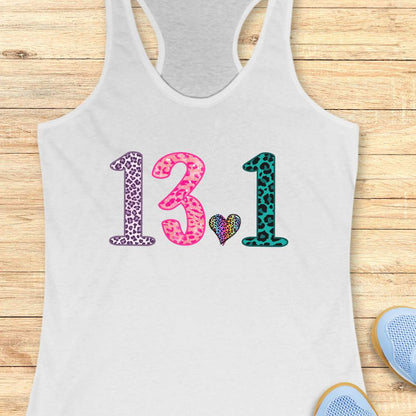 A white racerback tank top laid flat on a light wood background, featuring the numbers '13.1' in leopard print patterns (purple, pink, and teal) with a small multicolor heart between them.