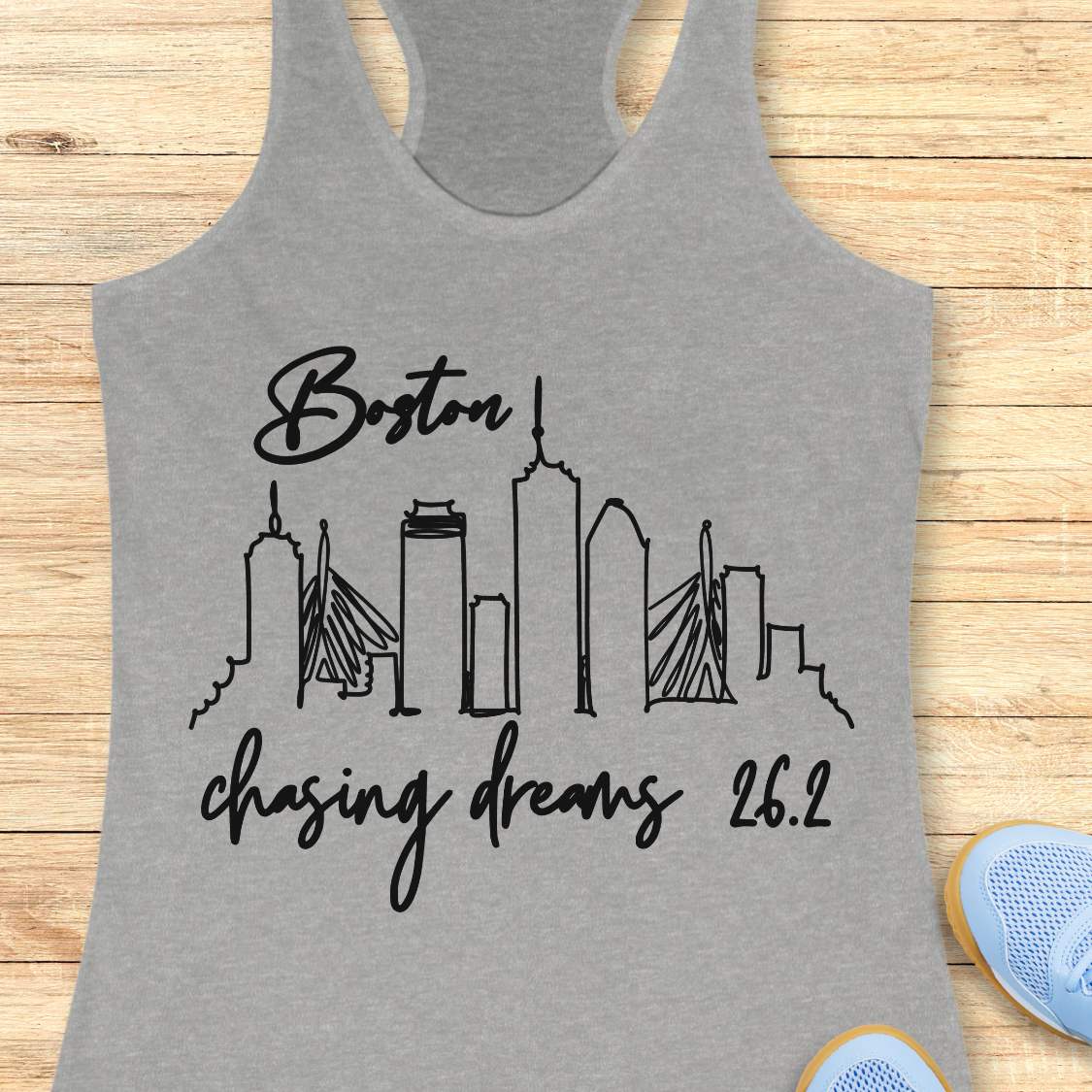 Gray tank top with black 'Boston chasing dreams 26.2' design on a wooden surface