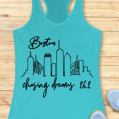 Turquoise tank top with black skyline design and text Boston chasing dreams 26.2, on a wooden surface