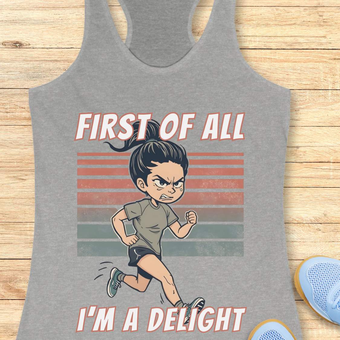 Gray tank top with cartoon character and text 'First of all I'm a delight' on a wooden surface