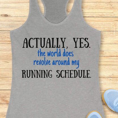 Gray tank top with humorous text 'Actually, yes. the world does revolve around my running schedule.' on a wooden surface