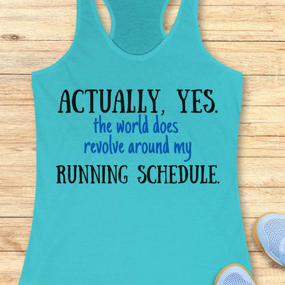 Turquoise tank top with humorous text 'Actually, yes. the world does revolve around my running schedule.' on a wooden surface