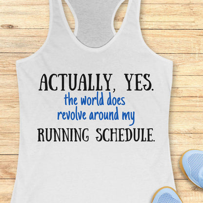 white tank top with humorous text 'Actually, yes. the world does revolve around my running schedule.' on a wooden surface