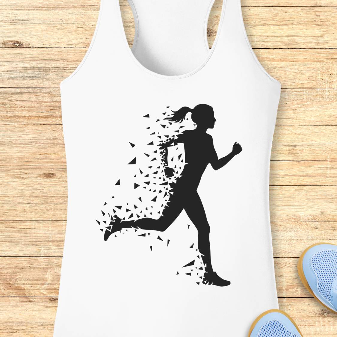 A white racerback tank top laid flat on a light wood surface, featuring a black graphic of a running woman whose body dissolves into small fragments. Partial blue sneakers are visible at the bottom right edge.