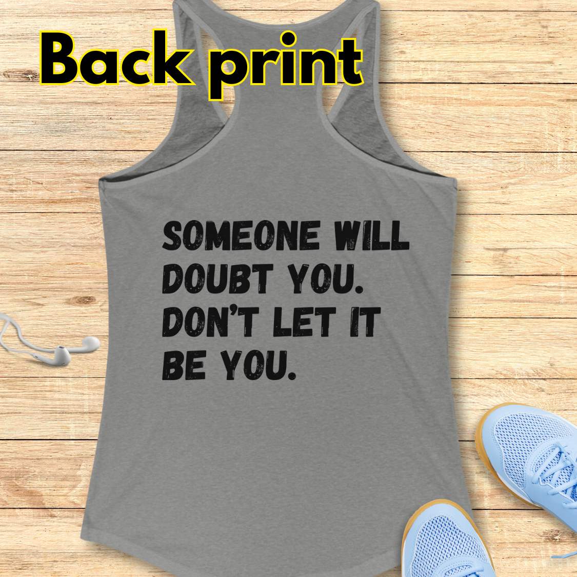 a grey tank op with a text at the back of the tank top "Someone will doubt you. Don't let it be you." on a wooden background