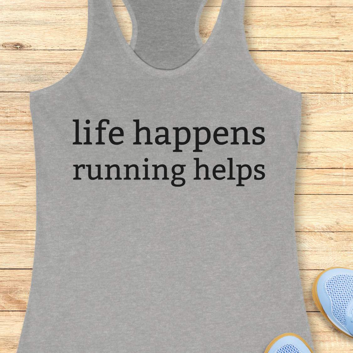 Gray tank top with 'life happens running helps' text on a wooden surface