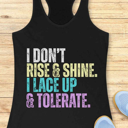 Printed black tank top featuring distressed white, yellow, light blue, and lavender text that reads 'I DON'T RISE & SHINE. I LACE UP & TOLERATE' displayed on a light wooden background with light blue sneakers at the bottom right