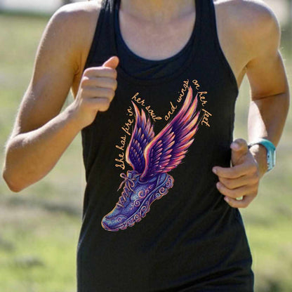 Photograph of a woman running outdoors in a black tank top with a vibrant graphic of a winged running shoe featuring colorful purple, orange, and pink wings, intricate blue scrollwork, and the text 'She has fire in her soul and wings on her feet'