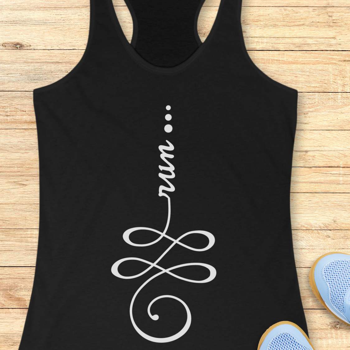 A black racerback tank top with a white graphic print that spells 'run' in script and infinity-style loops, laid flat on a light wood plank surface with partial blue sneakers visible at the bottom right.