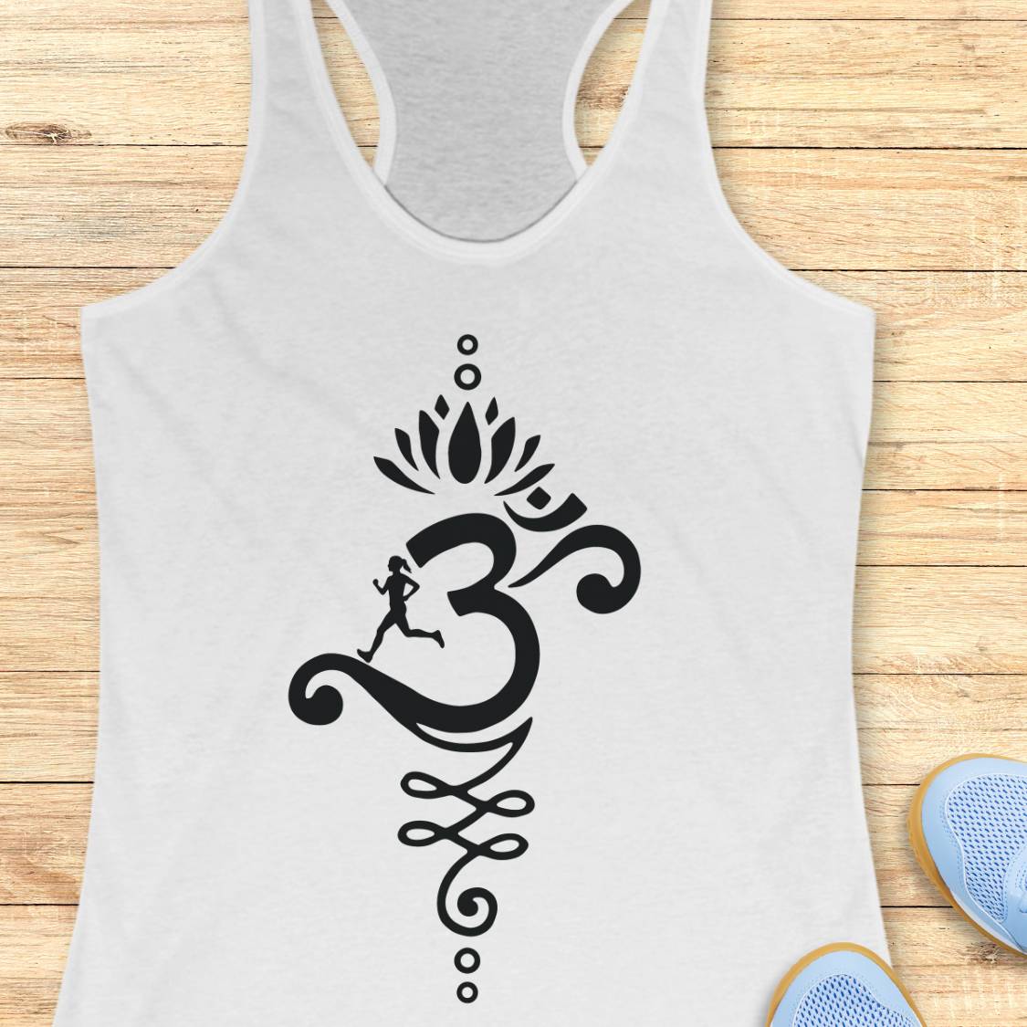 A white racerback tank top with a black Om symbol graphic featuring a running figure and lotus motif, displayed flat on a light wood background with blue shoes partially visible at the bottom right.