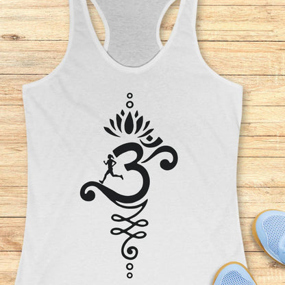 A white racerback tank top with a black Om symbol graphic featuring a running figure and lotus motif, displayed flat on a light wood background with blue shoes partially visible at the bottom right.