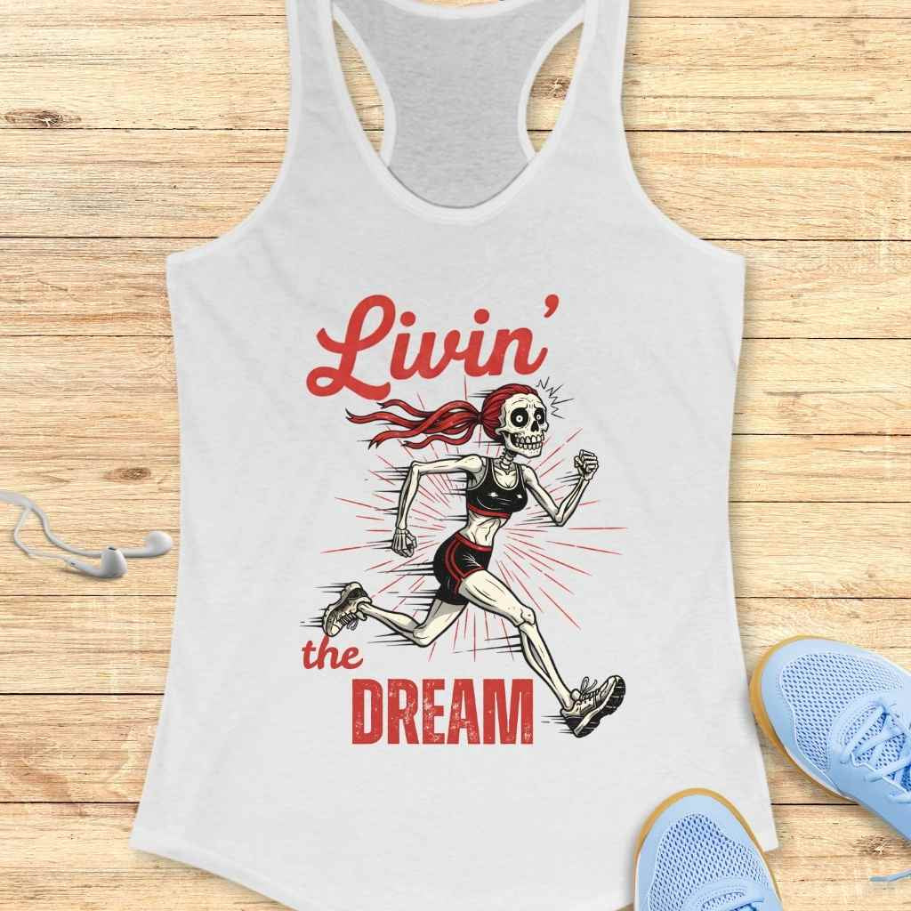 Graphic design on a white tank top depicting a skeleton woman with a red ponytail running in a black sports bra and shorts, surrounded by red sunburst lines and the red script text Livin' the Dream