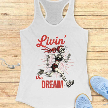 Graphic design on a white tank top depicting a skeleton woman with a red ponytail running in a black sports bra and shorts, surrounded by red sunburst lines and the red script text Livin' the Dream