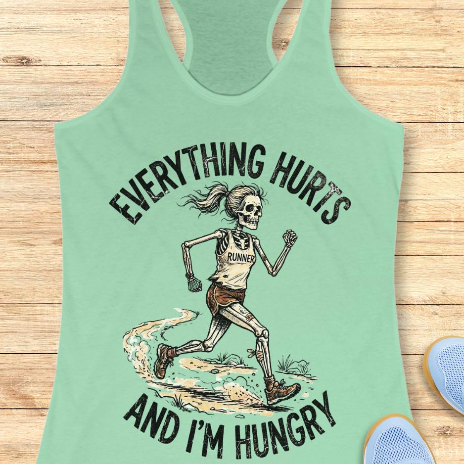 mint tank top with skeleton runner graphic and text 'Everything hurts and I'm hungry' on a wooden surface.