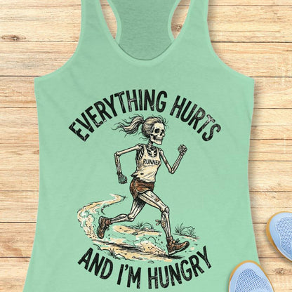 mint tank top with skeleton runner graphic and text 'Everything hurts and I'm hungry' on a wooden surface.
