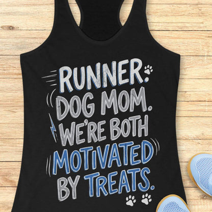A black racerback tank top laid flat on a light wood background, featuring the printed phrase 'RUNNER DOG MOM WE're BOTH MOTIVATED BY TREATS' in black and mustard yellow lettering with small paw print and lightning bolt accents. Partial blue shoes are visible at the bottom right as styling props.