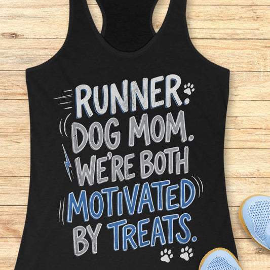 A black racerback tank top laid flat on a light wood background, featuring the printed phrase 'RUNNER DOG MOM WE're BOTH MOTIVATED BY TREATS' in black and mustard yellow lettering with small paw print and lightning bolt accents. Partial blue shoes are visible at the bottom right as styling props.