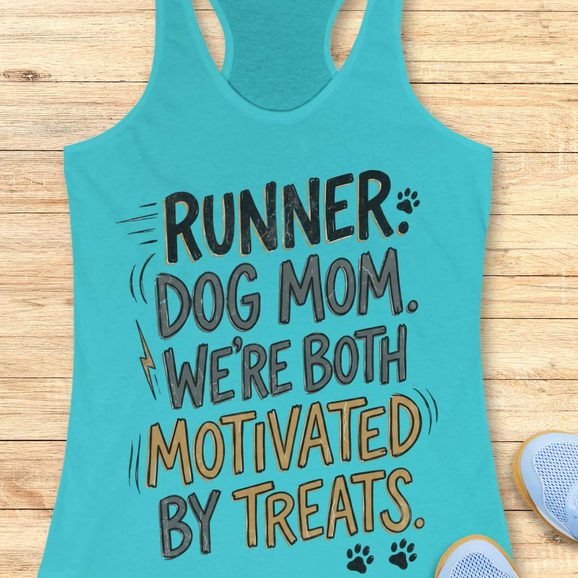 A turquoise racerback tank top laid flat on a light wood surface, printed with the phrase 'RUNNER DOG MOM WE'RE BOTH MOTIVATED BY TREATS.' in dark gray and tan lettering with small paw print and lightning bolt accents.