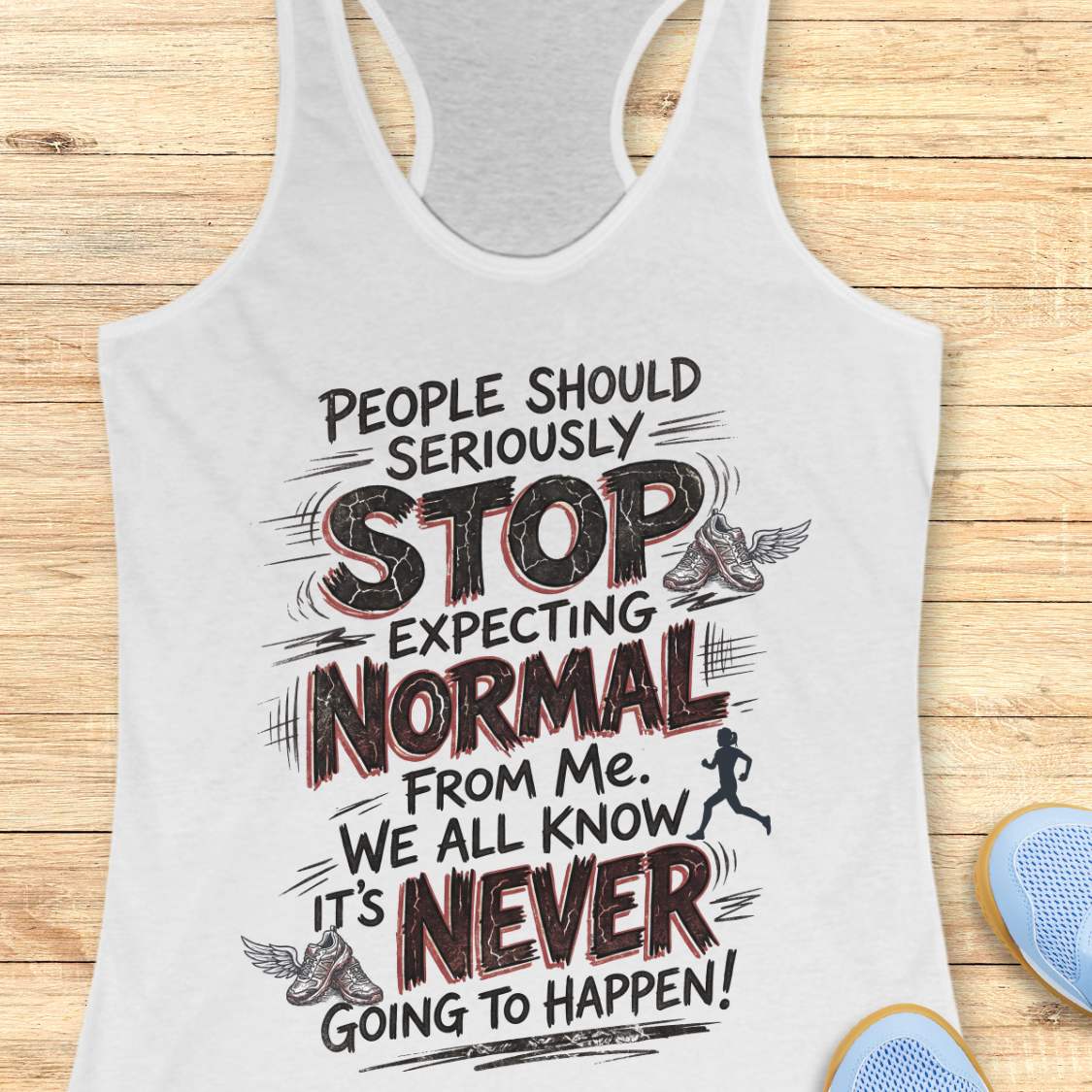 A white racerback tank top with a humorous graphic print, displayed flat on a light wood background with blue athletic shoes partially visible in the corner.