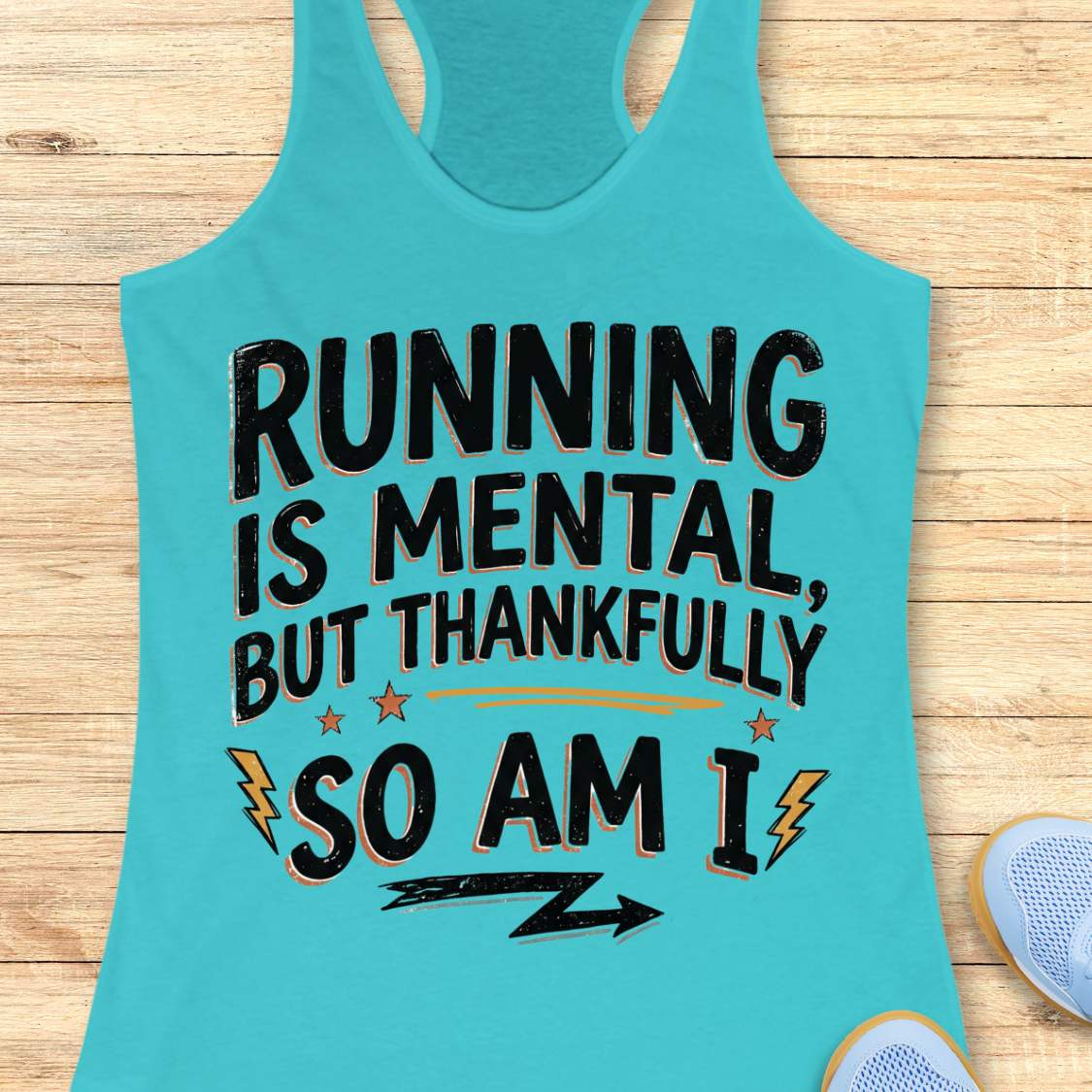 A turquoise racerback tank top laid flat on a light wood surface, featuring the printed phrase “RUNNING IS MENTAL, BUT THANKFULLY SO AM I” in black with small orange and yellow accents. A partial light blue shoe is visible at the lower right edge.