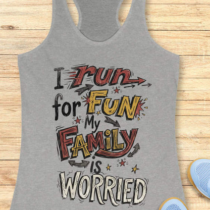 A heather gray racerback tank top with a colorful graphic text print reading 'I run for FUN my FAMILY is WORRIED' in red, yellow, black, and white lettering, displayed flat on a light wood background with partial blue shoes visible at the bottom right.