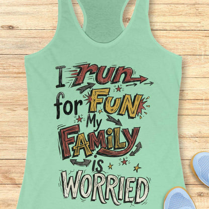 A mint green racerback tank top with a colorful graphic text print reading 'I run for FUN My FAMILY is WORRIED' in red, yellow, black, and white lettering, displayed flat on a light wood plank background with partial blue sneakers visible at the bottom right.