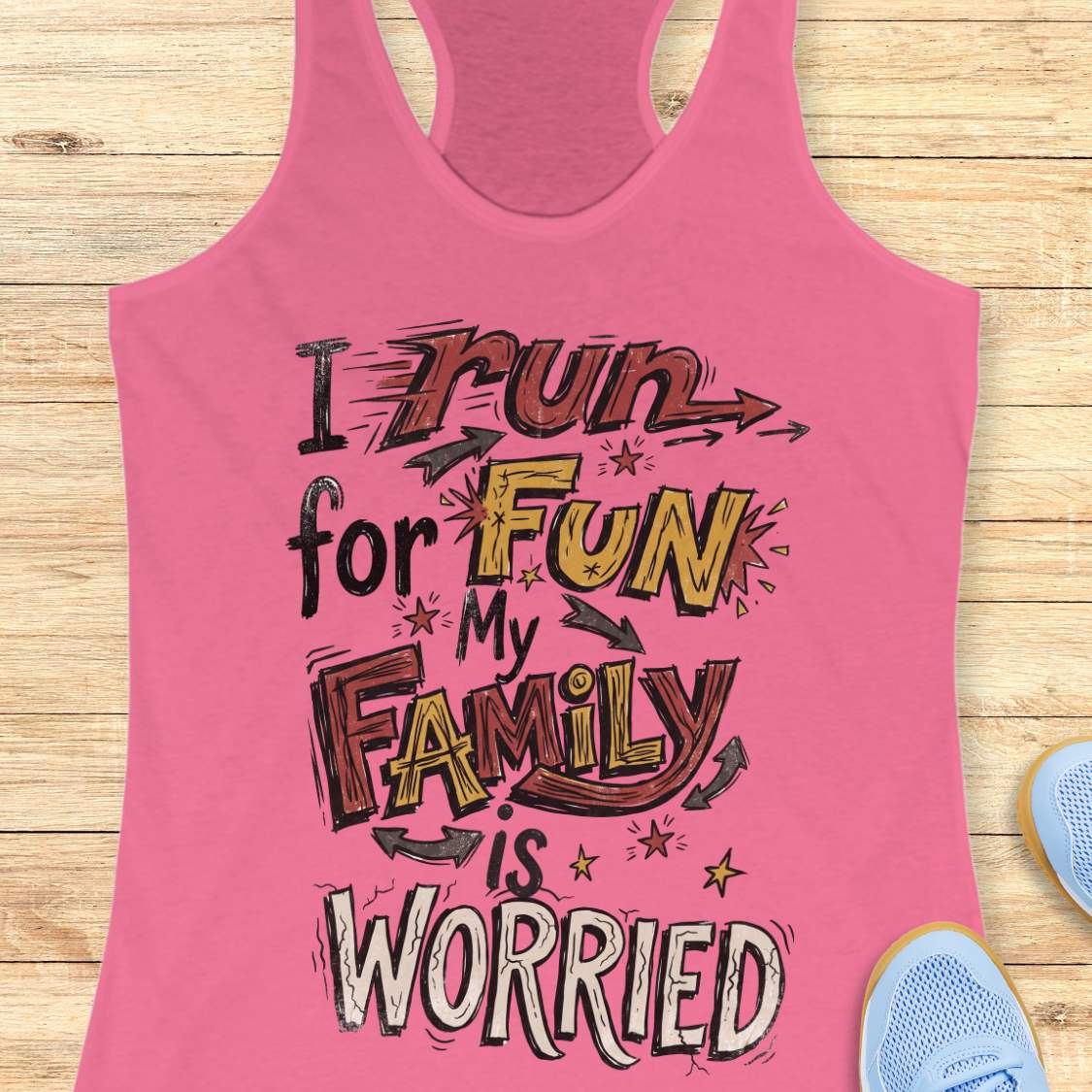 A pink racerback tank top laid flat on a light wood background, featuring a large hand-drawn style graphic that reads 'I run for FUN My FAMILY is WORRIED' in black, yellow, and white lettering. Partial blue sneakers are visible at the bottom right as styling props.