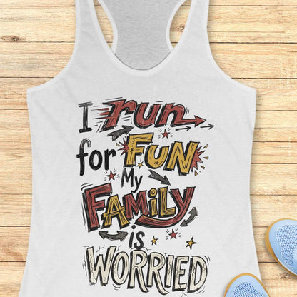 A white racerback tank top with a colorful graphic text that reads 'I run for FUN My FAMILY is WORRIED' in red, yellow, and black stylized lettering, displayed flat on a light wood background with partial blue shoes visible at the bottom right.