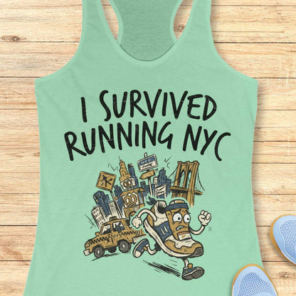 A mint green racerback tank top laid flat on a light wood background, featuring a graphic print that reads 'I SURVIVED RUNNING NYC' above an illustrated sneaker running past a city skyline and taxi cab. Part of a blue shoe is visible at the bottom right.