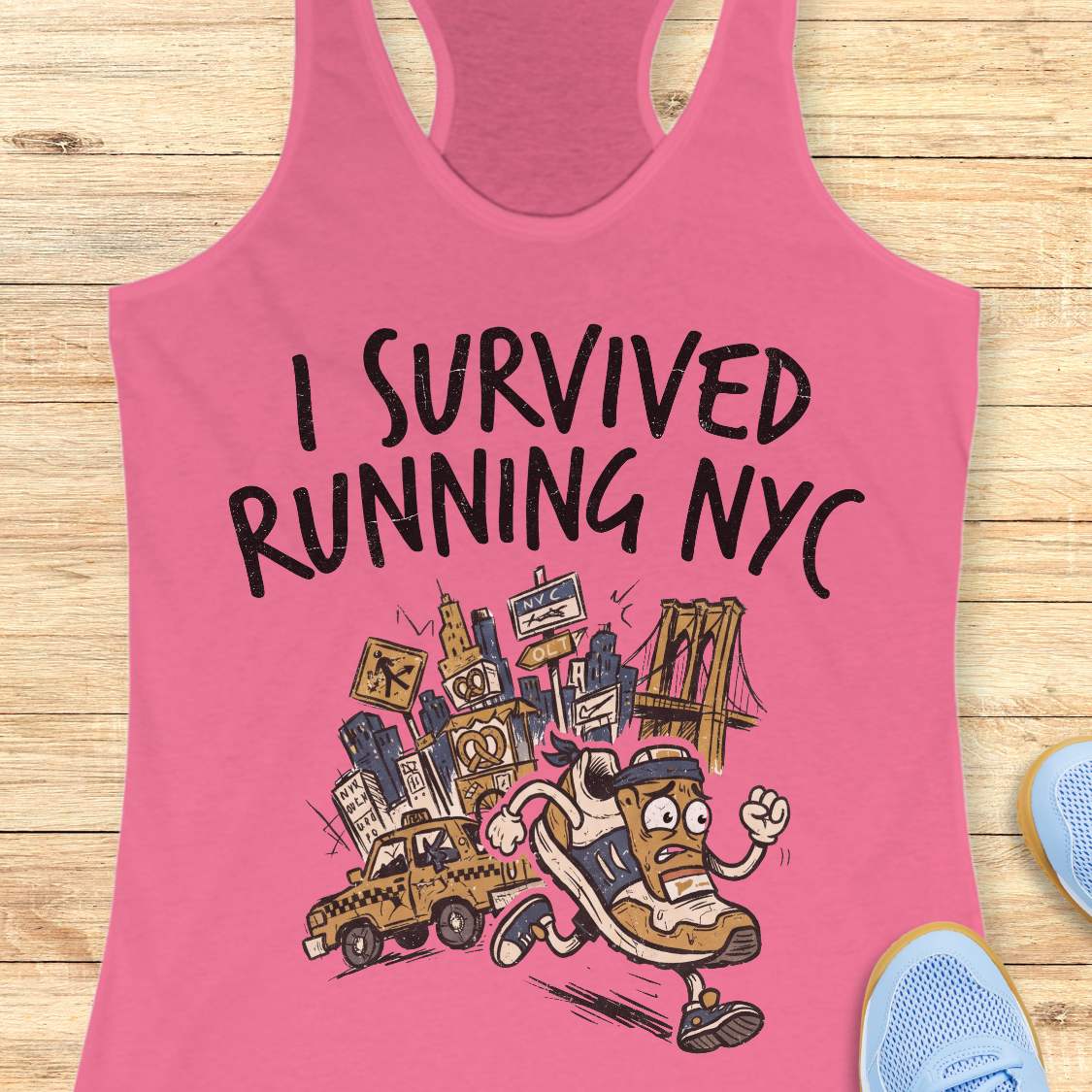 A pink racerback tank top laid flat on a light wood background, featuring a graphic illustration of a running sneaker and city elements with the text 'I SURVIVED RUNNING NYC'. Partial blue sneakers are visible at the bottom right as styling props.