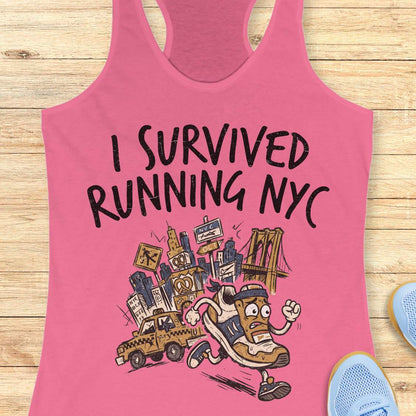 A pink racerback tank top laid flat on a light wood background, featuring a graphic illustration of a running sneaker and city elements with the text 'I SURVIVED RUNNING NYC'. Partial blue sneakers are visible at the bottom right as styling props.