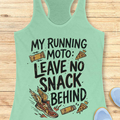 A mint green racerback tank top with a humorous graphic print reading 'MY RUNNING MOTO: LEAVE NO SNACK BEHIND' in black text, decorated with illustrations of a winged running shoe, a slice of pizza, and candy bars. The tank top is laid flat on a light brown wooden plank background, with partial blue sneakers visible in the bottom right corner.