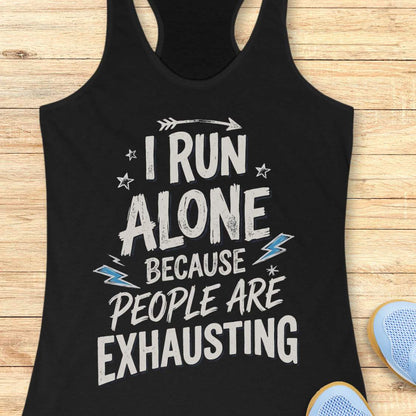 A black racerback tank top laid flat on a light wood background, featuring a distressed white graphic that reads 'I RUN ALONE BECAUSE PEOPLE ARE EXHAUSTING' with small blue lightning bolt accents. Part of a blue shoe is visible at the bottom right.
