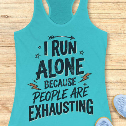 A turquoise racerback tank top laid flat on a light wood surface, featuring the printed text 'I RUN ALONE BECAUSE PEOPLE ARE EXHAUSTING' in dark lettering with small orange lightning bolt and star accents. Partial shoes are visible at the bottom right as styling props.