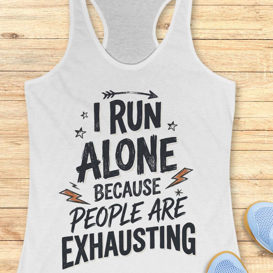 A white racerback tank top laid flat on a light wood background, featuring the distressed black text 'I RUN ALONE BECAUSE PEOPLE ARE EXHAUSTING' with small orange lightning bolt accents. Partial blue shoes are visible at the bottom right edge.