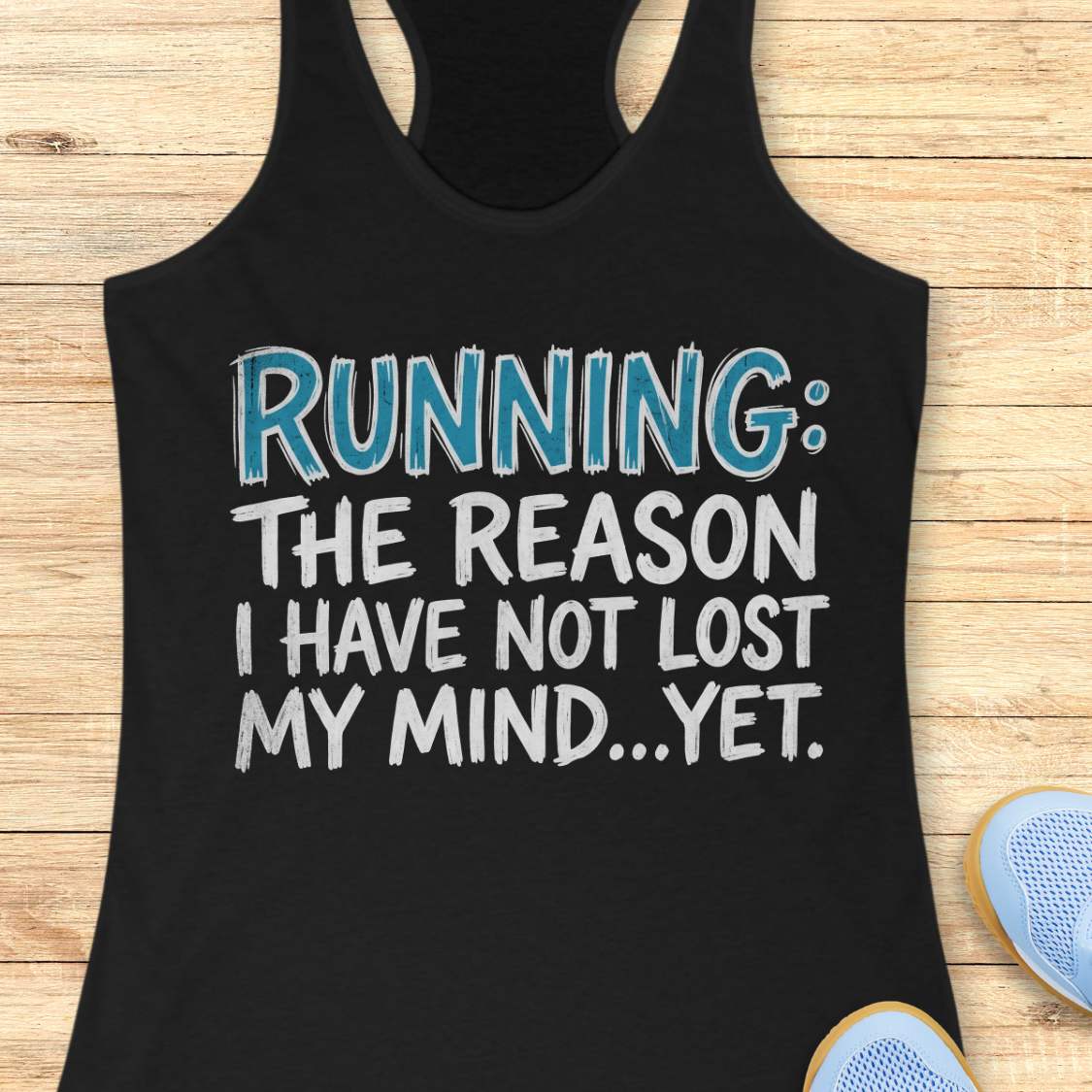 A black racerback tank top laid flat on a light wood background, featuring the text 'RUNNING: THE REASON I HAVE NOT LOST MY MIND.