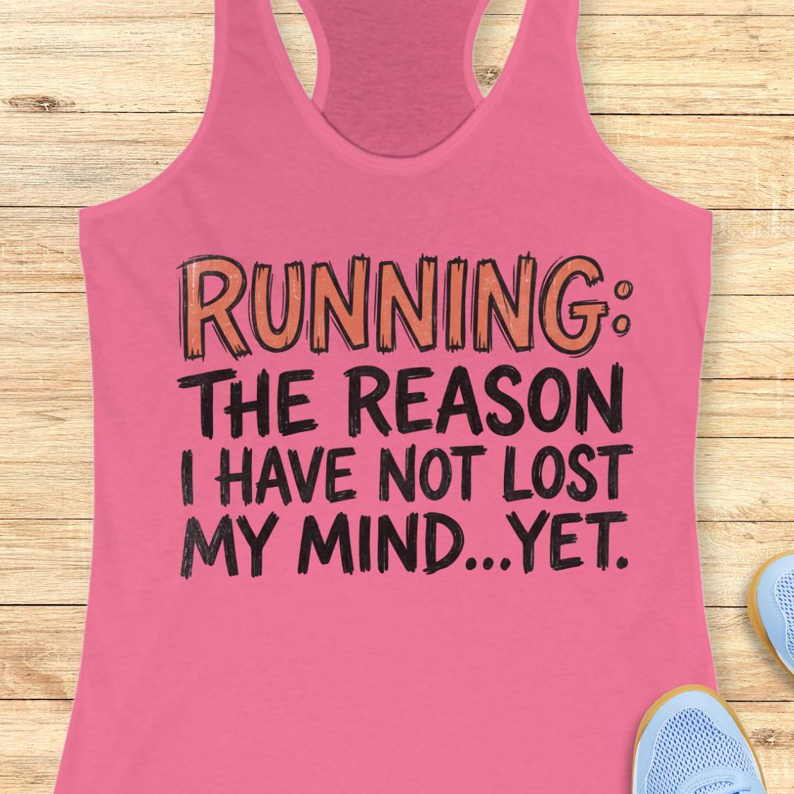 A pink racerback tank top laid flat on a light wood background, featuring the printed text 'RUNNING: THE REASON I HAVE NOT LOST MY MIND.