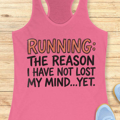 A pink racerback tank top laid flat on a light wood background, featuring the printed text 'RUNNING: THE REASON I HAVE NOT LOST MY MIND.
