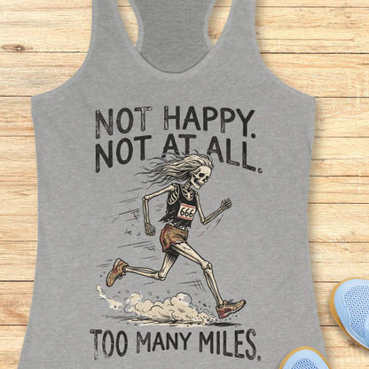 A heather gray racerback tank top laid flat on a light wood surface, featuring a distressed black graphic of a running skeleton with the text 'NOT HAPPY. NOT AT ALL.