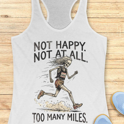 A white racerback tank top laid flat on a light wood background, featuring a black graphic of a running skeleton with the text 'NOT HAPPY. NOT AT ALL.