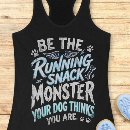 A black racerback tank top laid flat on a light wood background, featuring a humorous graphic that reads 'BE THE RUNNING SNACK MONSTER YOUR DOG THINKS YOU ARE.' in white and light blue lettering with paw prints, wings, and lightning accents.