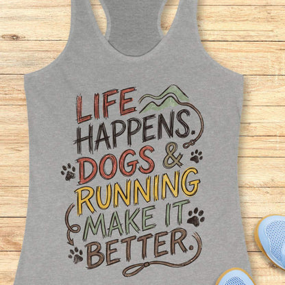 A heather gray racerback tank top laid flat on a light wood background, featuring a colorful graphic that reads 'LIFE HAPPENS. DOGS & RUNNING MAKE IT BETTER.