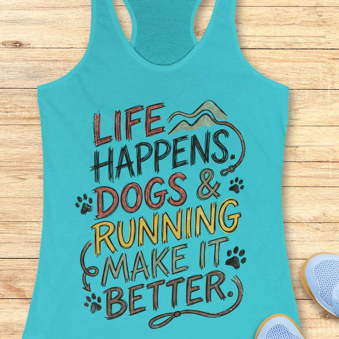 A turquoise racerback tank top laid flat on a light wood surface, featuring the printed phrase “LIFE HAPPENS. DOGS & RUNNING MAKE IT BETTER.