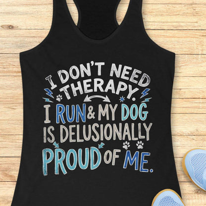 A black racerback tank top laid flat on a light wood surface, featuring the text 'I DON'T NEED THERAPY. I RUN & MY DOG IS DELUSIONALLY PROUD OF ME.