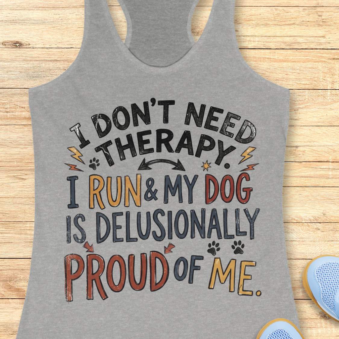 A heather gray racerback tank top with a colorful graphic text that reads 'I DON'T NEED THERAPY. I RUN & MY DOG IS DELUSIONALLY PROUD OF ME.